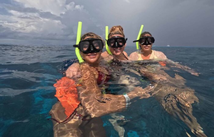 Trois amies portant des masques de plongée et des tubas prennent un selfie à la surface de l'eau claire des Caraïbes au large de Cozumel.