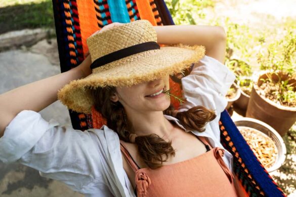 Femme se détendant dans un hamac coloré au Mexique, portant un chapeau de paille et souriant avec un brin d’herbe.
