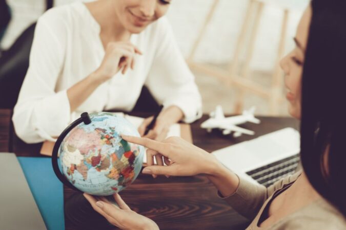 Une cliente pointe un globe terrestre du doigt pour discuter des prestations d'une agence de voyage.